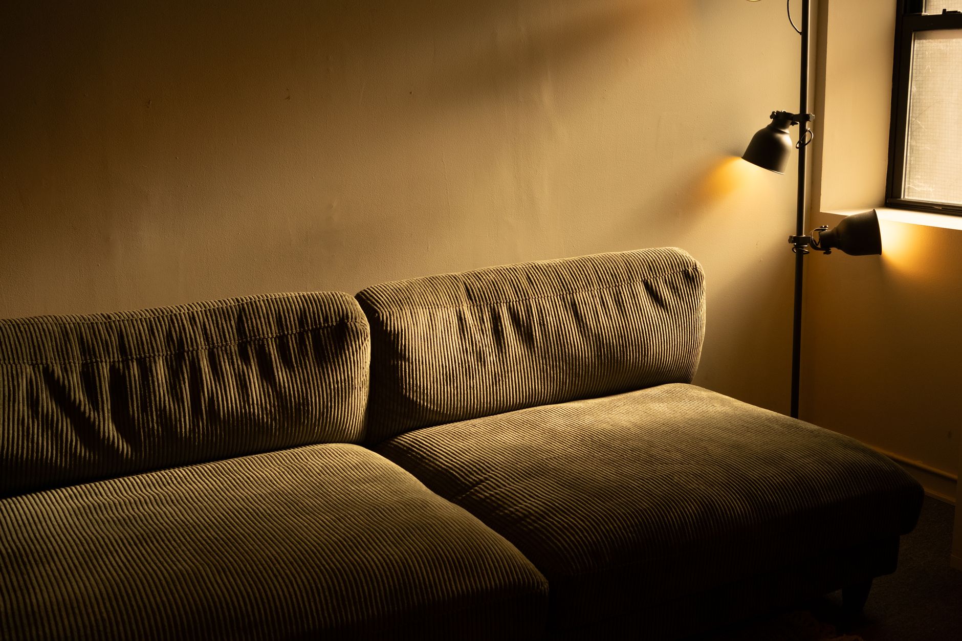 Warm verlichte woonkamer met een ribstof bank tegen een gladde, lichte wand